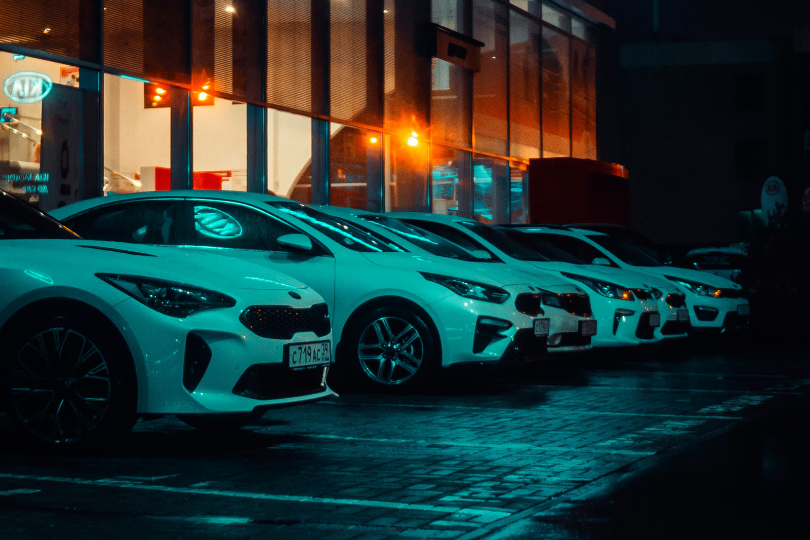 A row of identical white cars lined up outside a dealership showroom